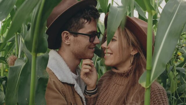 Portrait of hipster newlywed couple in brown hats enjoying relationship with each other. Pretty blonde girl snuggling up to caucasian young man, petting and touching his face, huging and kissing him.