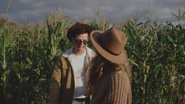 Close up of hipster girl in brown hat leading young millennial man through field with crops. Guys spending time together on date outside city. Little trip or travel in countryside. Family concept.