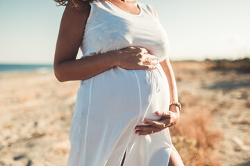 Giovane donna incinta con vestito bianco vicino al mare