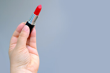 close-up female hand holding a tube with new bright red lipstick on a gray background, wants to do...