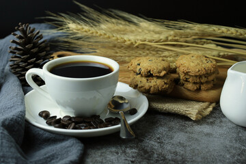 Black coffee in a white cup with cookies made from oatmeal with blackcurrant in hemp sackcloth and black background.
