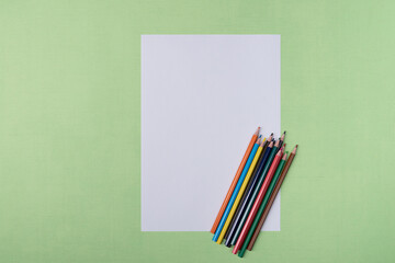 A blank white sheet and colored pencils for drawing on a plain textured background with space for copying and lettering.