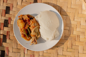 Traditional African food dish made from cornmeal porridge and chicken curry stew - obrazy, fototapety, plakaty