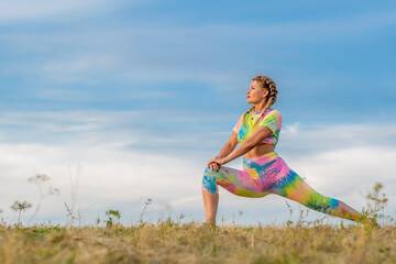 Young girl in bright tracksuit performs exercise to stretch muscles of legs. Long forward lunge....