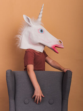 Unrecognizable child in unicorn mask against armchair