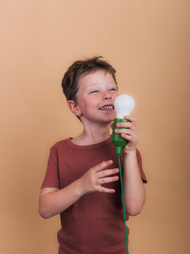 Smiling boy with decorative light bulb on beige background