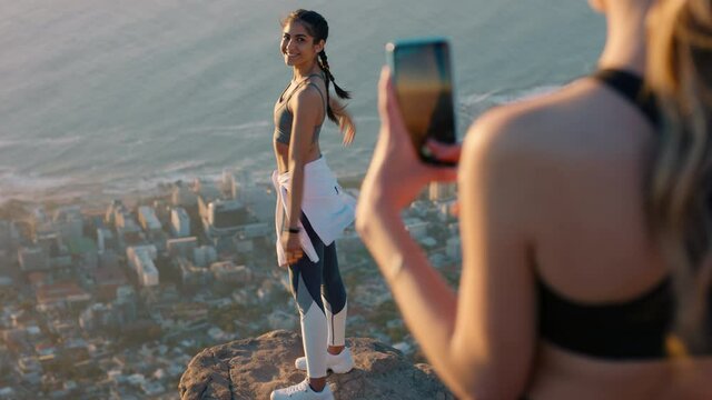 girl friends taking photo on mountain top using smartphone camera happy young woman posing for friend with mobile phone sharing hiking adventure on social media