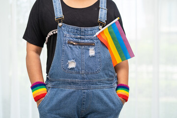 Asian lady wearing blue jean jacket or denim shirt and holding rainbow color flag, symbol of LGBT...