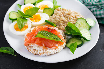 Breakfast oatmeal porridge with boiled eggs, salmon sandwich and cucumbers salad. Healthy food. Lunch.