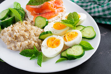 Breakfast oatmeal porridge with boiled eggs, salmon sandwich and cucumbers salad. Healthy food. Lunch.