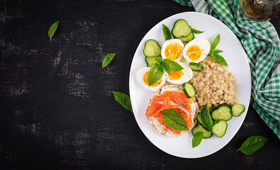Breakfast oatmeal porridge with boiled eggs, salmon sandwich and cucumbers salad. Healthy food. Lunch. Top view, flat lay