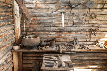 Interior view of the old village forge. On the wooden workbench and the walls there are metal tools of the blacksmith.