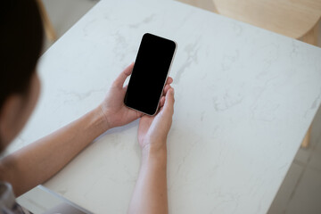 Top view mockup image of a woman holding a black mobile phone with blank black desktop screen