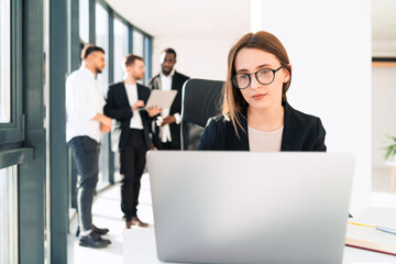 Woman working in the office behind a laptop and her work colleagues in the background