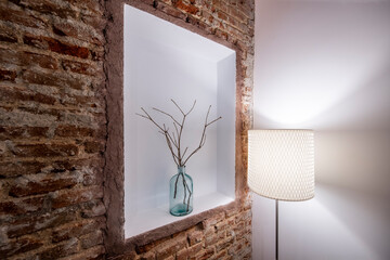 Niche in the exposed brick wall of a vacation rental apartment with decoration of dry branches and blue vase