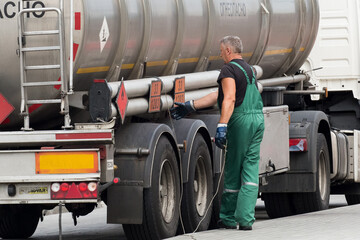 Belarus, Gomel region - August 21, 2020: A truck driver in overalls grasps the grounding cord or wire to ground the machine. Transportation and delivery of fuel and gasoline. Oil and gas cargo