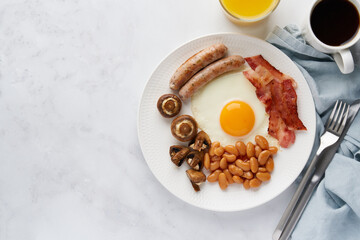 Horizontal of classic irish morning breakfast. Tasty keto diet meal. Sausages, mushrooms, kidney beans, eggs, bacon, orange juice and coffee on white background. Irish cuisine. Copy space