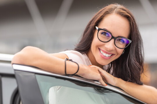 Happy new female car owner leans on the open door of the vehicle with a big smile