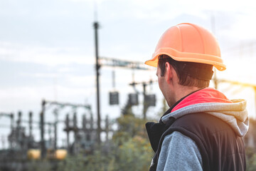 Worker in a helmet against the background of a substation and high-voltage poles