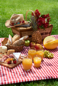 Cesta de pic-nic com p&atilde;es, queijos, frutas e sucos num gramado
