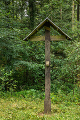 Genk, Belgium - August 11, 2021: Domein Bokrijk. Dark wooden cross with INRI sign but where Jesus has disappeared from on side of green forest. 