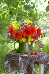 Still life in the summer garden with a cheerful red-yellow-purple bouquet of flowers in a green teapot