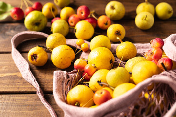 a lot of yellow pears spill out of a wicker mesh pink bag on a wooden table