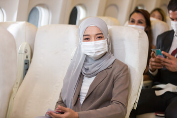 Asian Muslim business woman in hijab headscarf wearing protective face mask in airplane....