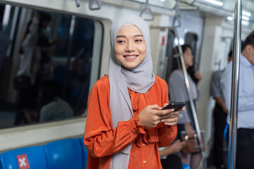 Asian muslim woman wear hijab head scarf and using mobile phone in the metro or train subway,...