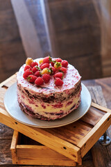 Chocolate raspberry cake with raspberry cheesecake layer. Decorated with berries. Side view, wooden boxes.