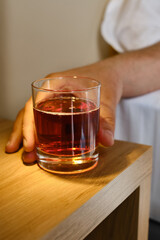 A glass of alcoholic drink in the hands of a close-up of a man. A man drinks alcohol in a hotel room or at home. Tasting spirits such as scotch, brandy or whiskey