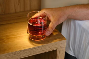 A glass of alcoholic drink in the hands of a close-up of a man. A man drinks alcohol in a hotel...