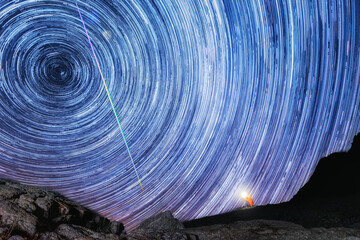 Male hiker sitting on the rocks far in the distance and admiring a 2D luminous spiral sky