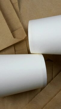 Empty paper package, eco-friendly disposable biodegradable packaging for goods, and empty paper cup. Rotates in circle. Eco friendly background. Vertical video. Top view.