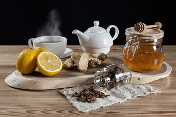 Honey in a jar, sliced lemons and ginger on a wooden rack. Next to it is hot tea in cups and cloth with sprinkled bee putty.  Home treatment for colds or flu. 