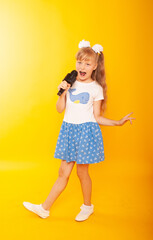 a little charming girl with a microphone in her hands depicts a song on a yellow background in isolation, back to school, vocal lesson