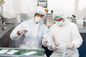 Naklejka premium male engineers wearing personal protective equipment uniform(PPE) wearing medical face mask, producing medical face masks and checking machine in laboratory