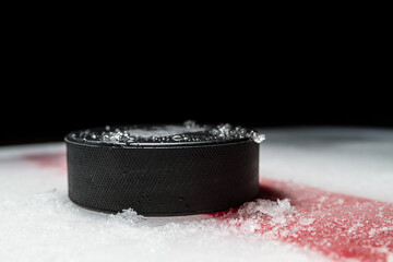 Black hockey puck on the ice rink, with painted red line. - obrazy, fototapety, plakaty