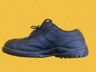 Safety shoe black on yellow floor. Modern working boots isolated from external influences.