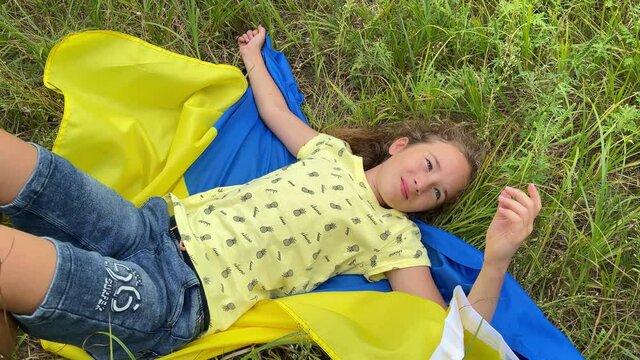 4k Smiling small girl lies on Ukrainian flag in the meadow