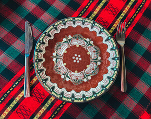 Traditional Bulgarian decorated ceramic empty plate on a red cloth, restaurant table. Fork and knife. - 454377854