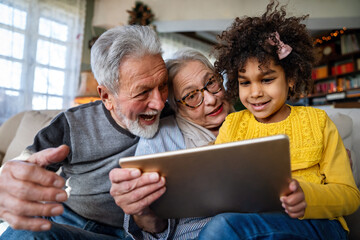 Portrait of happy grandparents with little girl using digital tablet at home