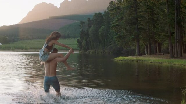happy couple splashing in lake at sunset young man picks up girlfriend splash in water having fun game enjoying romantic summer love