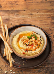Chickpea hummus in bowl with breadsticks on wooden table. Top view, copy space, selective focus.