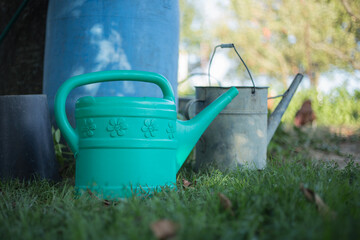 Watering can. New plastic and an old aluminum watering cans in grass in the garden on summer time. Close up of metal watering pot at summertime. Gardening background