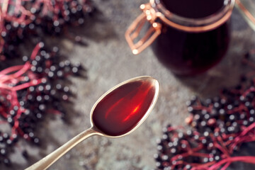 A spoon with black elder syrup made from fresh elderberries