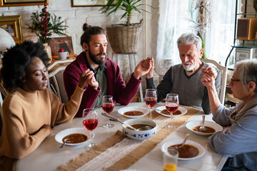 Family and religious concept. Group of multiethnic people with food praying before meal