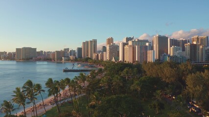 Naklejka premium Panning aerial drone slowly flying over a colorful Honolulu Skyline while Sunset in Oahu, Hawaii with Waikiki Beach Shooting from a bird's eye view. Magnificent mountains of Hawaiian island of Oahu.