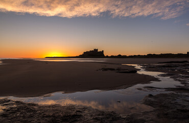Obraz premium The iconic Bamburgh Castle in Northumberland at sunrise, with the nearby beach deserted. 