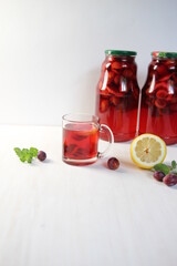 Glass of homemade compote of plums, lemon, mint on white background